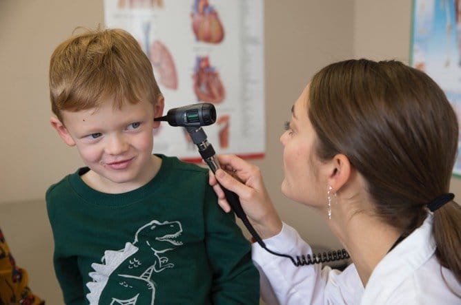 Family Nurse Practitioner examining pediatrics ear with auriscope