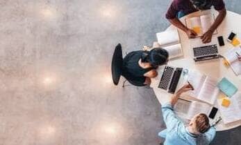 birds eye view of students working at a round table with laptops and study materials