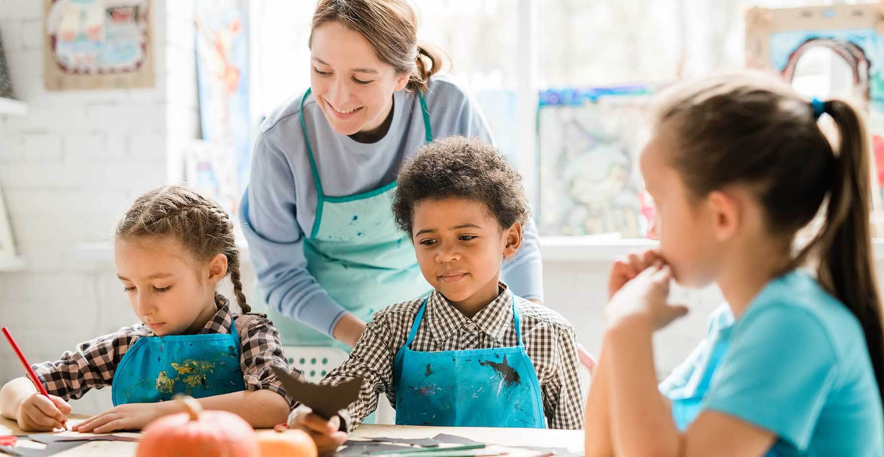 Children in aprons painting with teacher