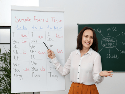 Young woman standing at a white board appearing to teach another language to a room of people.