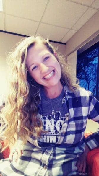 This is a photo of our featured AA Communication student, Angela. She is smiling and has long curly blonde hair. She is wearing a flannel shirt.
