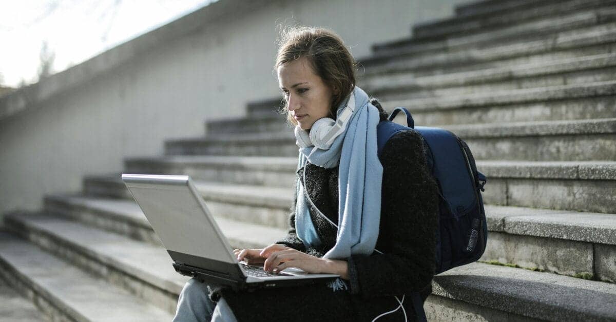 Female student reading on her laptop while sitting on steps outside