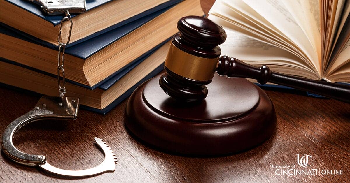A gavel, a stack of books, and a pair of handcuffs sit on a brown desk.