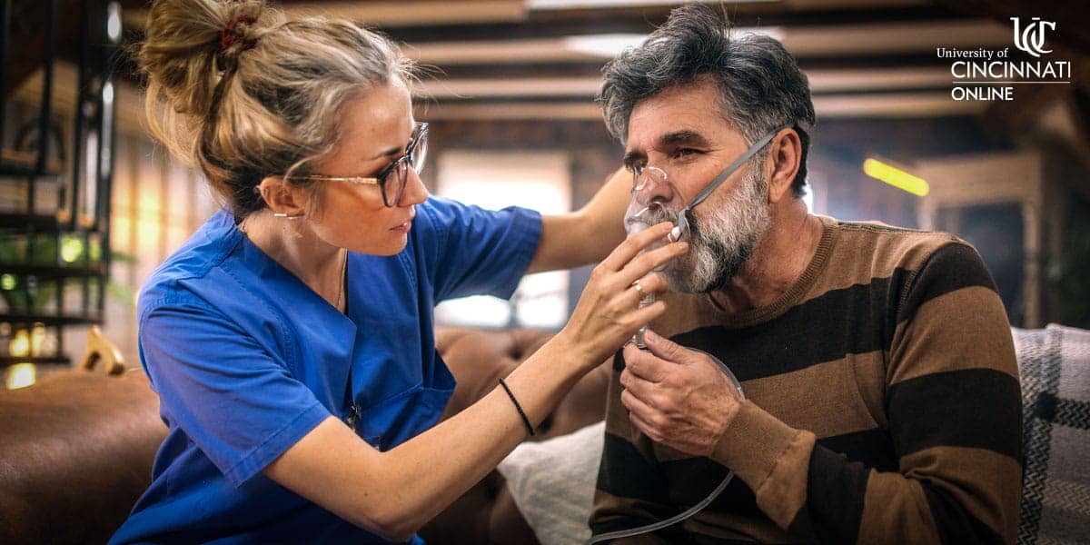 A female respiratory therapy professional holds a respiratory mask over a male patient's mouth and nose.