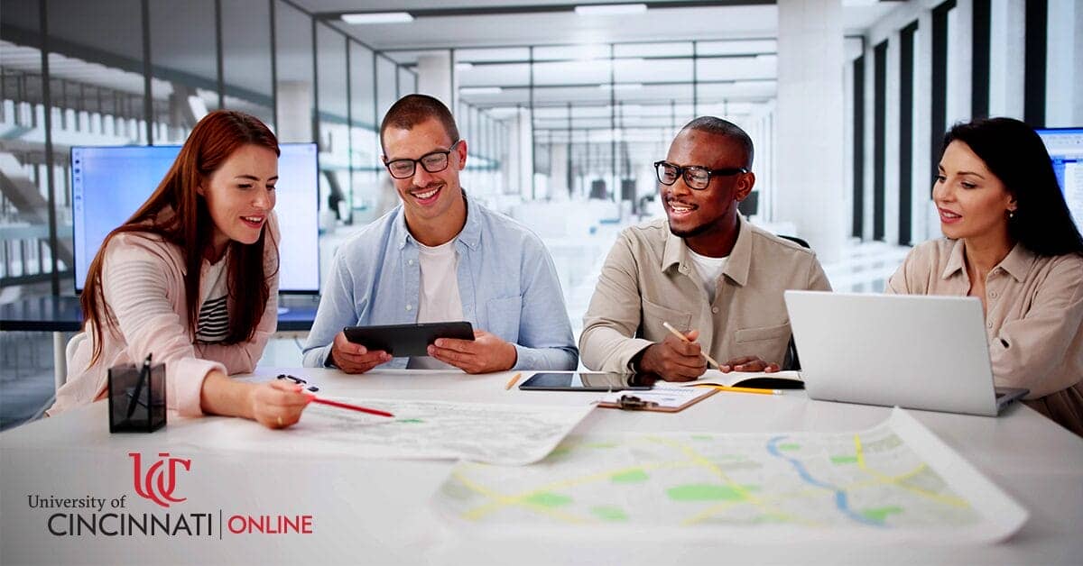 Four city planning professionals sit around a table. There are maps and papers on the table for an urban development project. They sit in a brightly lit office space.
